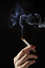 finger holding burning cigarette against dark