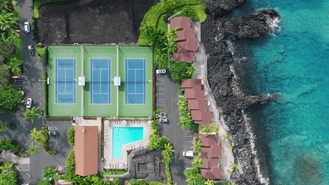 Still drone shot above empty tennis court at black lava rocky coast. Background of tennis court in tropical lavish green garden of resort hotel area. Big Island, Hawaii USA summer trip 4K vacation