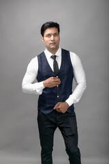 Studio shot of cheerful, young, handsome Indian business man in formal wear against grey background. Male model. Fashion Portrait.