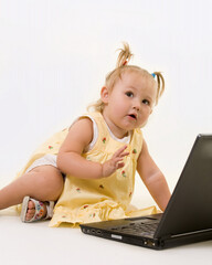 Adorable baby girl toddler in pigtails sitting on the floor working on a laptop computer