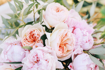 A woman, a bride holding a bridal bouquet of pastel coloured pale pink roses and peonies.