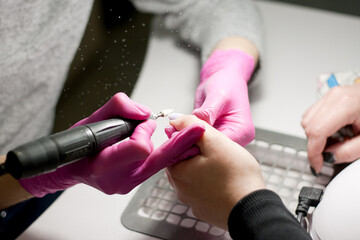 Salon manicure. Professional hardware manicure. Closeup of hands of manicurist in pink gloves uses electric drill to remove gel polish on hands during manicure. Dust when removing varnish.