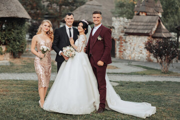 Wedding portrait. Front view of newlyweds walking hand in hand among friends. Girls in golden dresses hold bouquets, the bride in a voluminous dress, the groom and his friends in suits. 