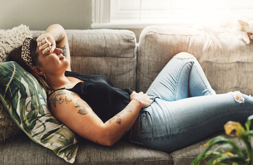 Obraz premium Period pain, menstrual and a woman on a sofa in the living room of her home suffering from cramps. Stomach, digestion and constipation with a young female person holding her abdomen in discomfort