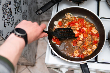 close-up on cooking chicken breast fillet with tomatoes and onions in a pan. Dinner preparation