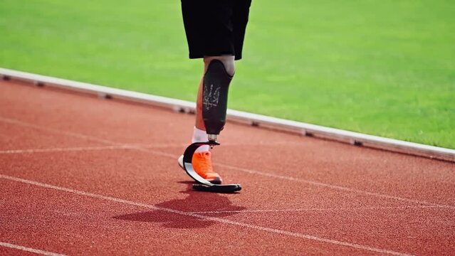 A disabled athlete with prosthetic legs is training at an outdoor stadium on a sunny day. An amputee runner is standing on the track. Motivational sports shots.
