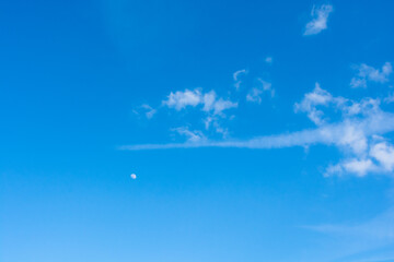 Fototapeta na wymiar księżyc i białe chmury na tle niebieskiego dziennego nieba