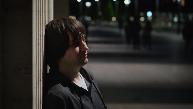 Abandoned, lonely, sad young man stands against the wall in the night city