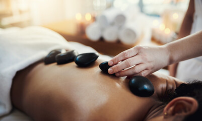 Woman, hands and rocks in back massage at spa for skincare, beauty or relaxation on bed indoors....