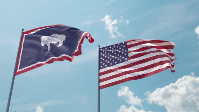 Wyoming flag and the USA flag on a flagpole realistic wave on strong wind in blue sky. State of Wyoming and The United States of America