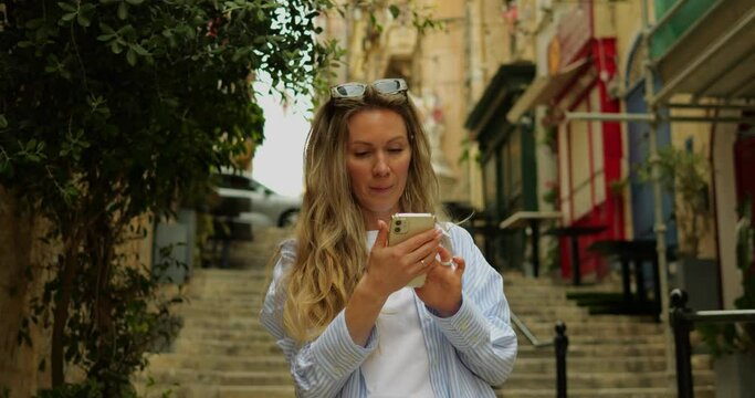 Young woman in sun glasses in city center old town swipe smartphone enjoy photo. Female adult on old stairs in downtown on summer day smile checks instant messages in social media on phone.