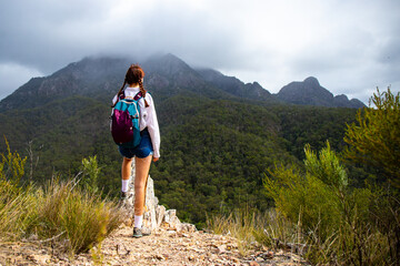 beautiful and brave girl standing at the top of the hill with large mountain in front of her; mighty mount barney in queensland, australia seen from yellow pinch lookout