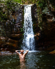 young man with beard and tattoos swimming in the rock pool under large tropical waterfall in mount barney national park, queensland, australia; hidden waterfall in the rainforest