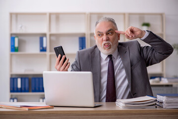 Old male employee speaking by phone at workplace