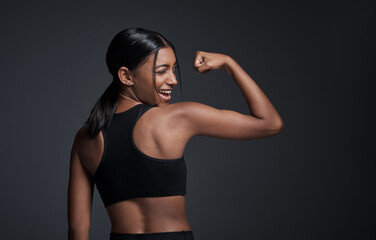 Fototapeta na wymiar Wink, happy and woman flexing muscle in studio isolated on a black background mockup. Strong flex, funny and Indian female athlete with bicep, arm strength or bodybuilder back, fitness or workout.