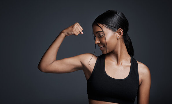 Sports, smile and woman flexing bicep in studio isolated on black background. Strong, happy and Indian female athlete with muscle, arm strength and bodybuilder ready for fitness, workout or exercise.