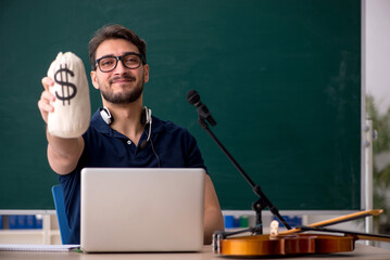 Young male music teacher holding moneybag in the classroom