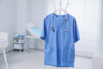 Blue medical uniform and stethoscope hanging on rack in clinic