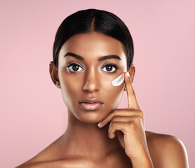 Portrait, skincare and face of woman with cream in studio isolated on pink background. Dermatology, creme cosmetics and serious Indian female model apply moisturizer lotion for skin health or beauty.