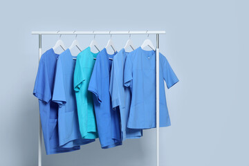 Obraz premium Different medical uniforms on rack against light grey background. Space for text
