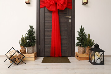 Wooden door with beautiful red bow near evergreen trees ,logs and lantern. Christmas decoration
