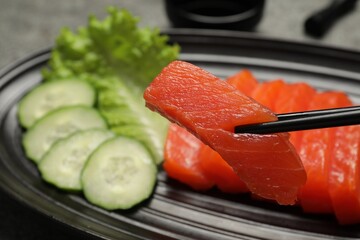 Taking tasty salmon slice with chopsticks from plate, closeup. Delicious sashimi dish
