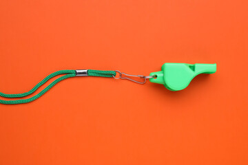 One green whistle with cord on orange background, top view