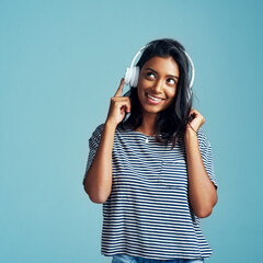 Woman, thinking and headphones with music in studio with happiness and web audio. Blue background, Indian female person and young model listening, hearing and streaming a song with smile and mockup