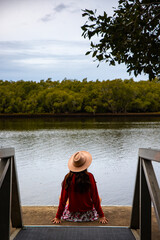 elegant woman in a hat sitting and relaxing by the river; meditation by the river in queensland, australia; bond with nature; 