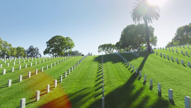 Peaceful eternity concept. Los Angeles National Cemetery California USA. Drone flying above scenic green field with rows of white grave plates. National cemetery where buried all members armed forces