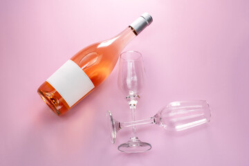 Wine bottle mockup, unopened bottle of rose wine and two glasses on pink background, top view, copy space, flat lay