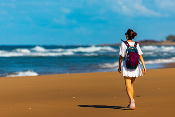 back view of a beautiful hiker girl in white dress walking on an endless beach in deepwater...