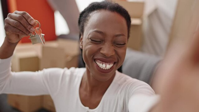 African american woman having video call holding keys at new home