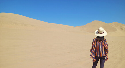 Female traveler looking at the beautiful sand dunes of Huacachina desert, Ica region, Peru, South...