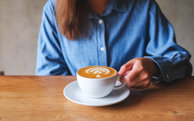 Closeup image of a woman holding a cup of latte coffee on wooden table