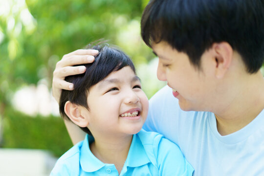 Happy lovely Asian father and son enjoy relaxing in picnic in the garden together, boy hugs his daddy.