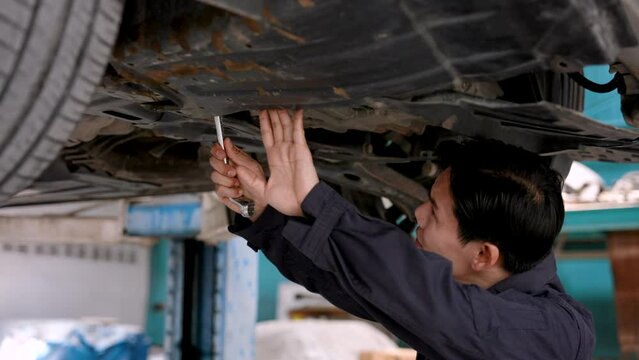 Asian mechanic checking under car High lift, look at the bottom of the car. Wrenches are being used to repair faults and damage caused by accidents. Prepare to repair to return to work as usual.