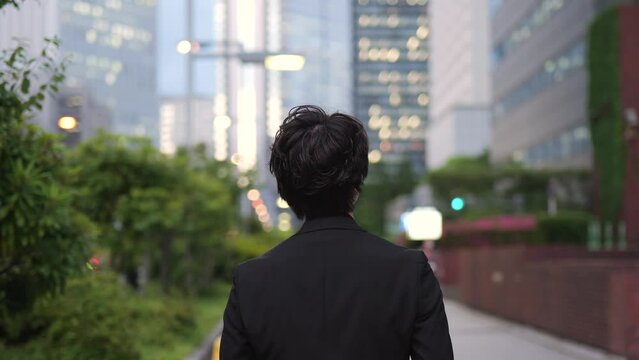 夜の新宿のビル街を歩く男の後ろ姿