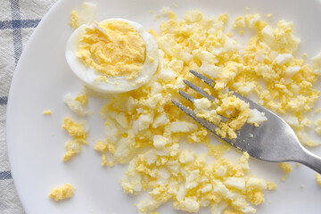 Mashed boiled egg with a fork on a white plate.  Selective focus at the egg on the fork.  Egg...