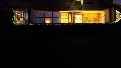A nighttime overhead view of a ship's cargo hold with white wrapped containers. drone view - Powered by Adobe