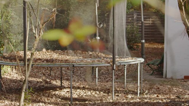 Old Trampoline With Dried Leaves On Mat Covere With Safety Nets In The Garden. - handheld