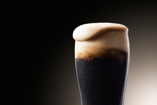 黒ビール、水滴のついたグラスから泡が溢れる冷えたビール Dark Stout Beer with Creamy Foam