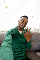 Portrait of happy african american gay man showing wedding ring while sitting on sofa in living room