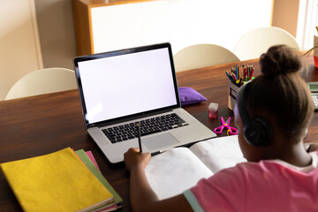African american girl doing schoolwork using laptop at home, copy space on screen