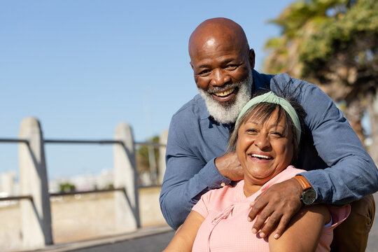 Portrait of happy senior african american couple embracing on promenade over palm trees