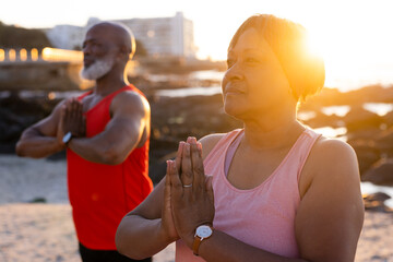 Happy senior african american couple practicing yoga and doing poses at beach