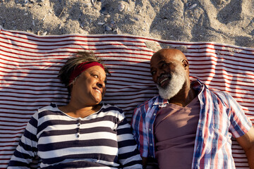 Happy senior african american couple lying on towels at beach