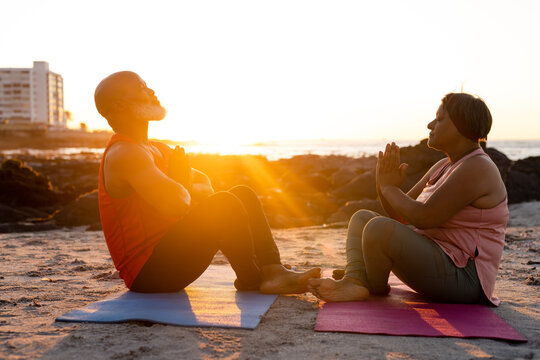 Happy senior african american couple practicing yoga on yoga mats at beach