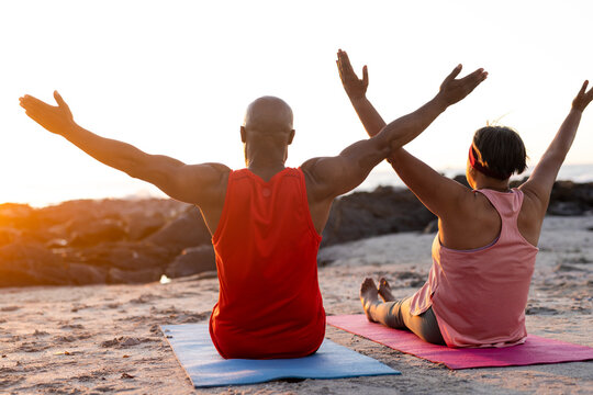 Senior african american couple practicing yoga on yoga mats with arms wide at beach