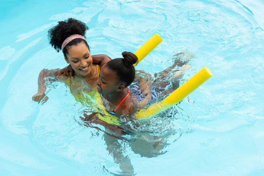 Happy african american mother teaching daughter to swim with float in swimming pool